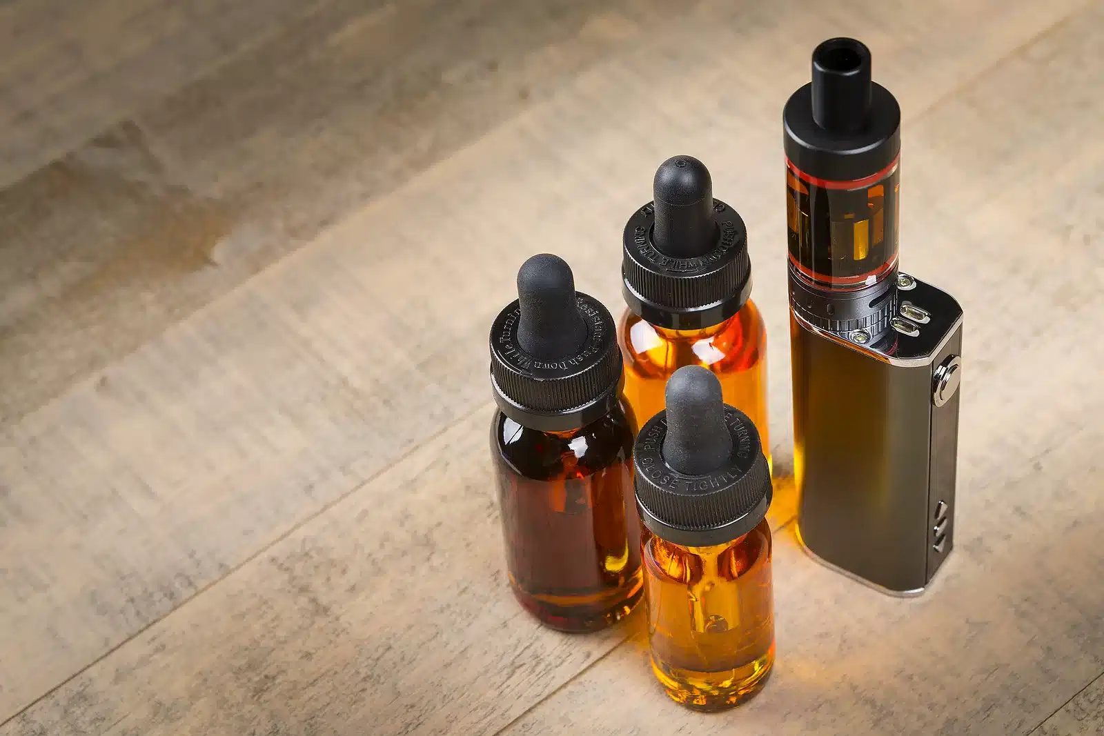 Vaping hardware and juice. Vape e-juice with mod and bottles with child proof lids over wood background.