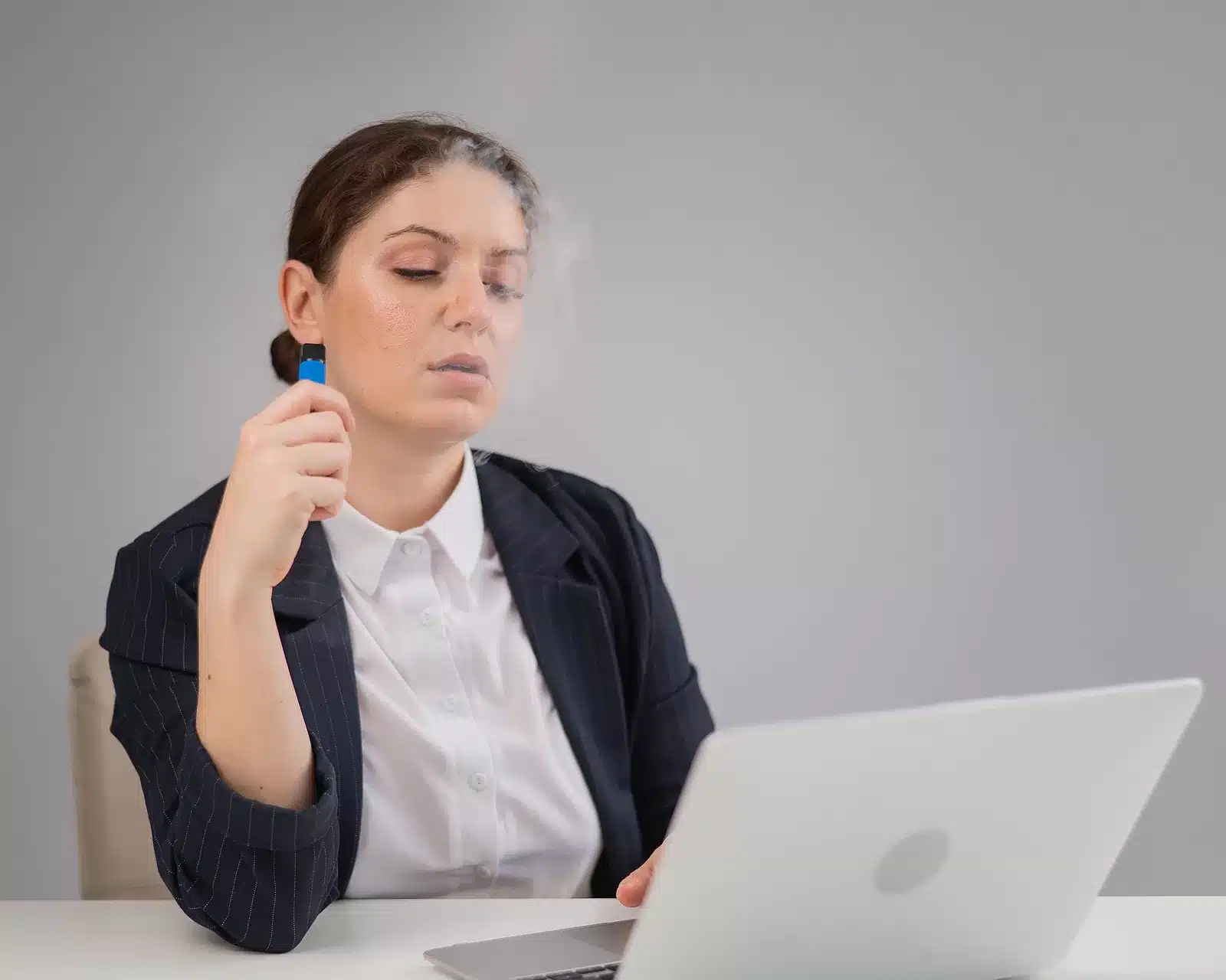 Business Woman Smoking A Disposable Vape While Sitting At Her De